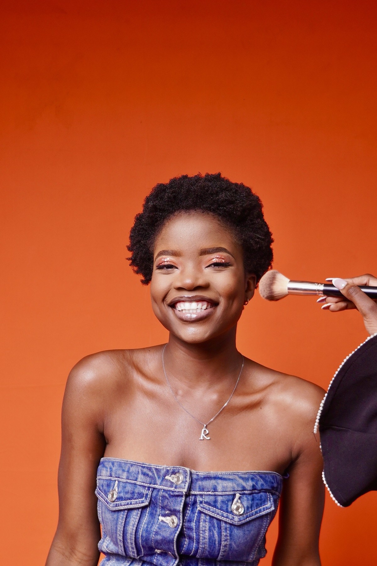 Glam Boutique makeup look with shimmering eyes and luminous skin against an orange backdrop